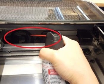 Using a can of compressed air to clean the largest circuit board located in the left-hand side of the Glowforge.