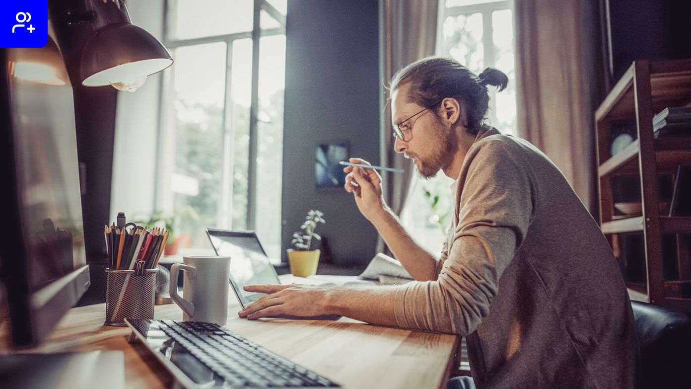 a man sitting at a desk in a home office environment, working on a laptop