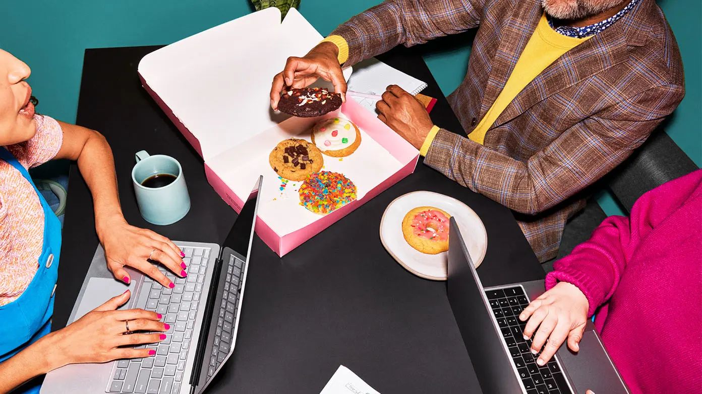 people gathered around table working on laptops and eating cookies