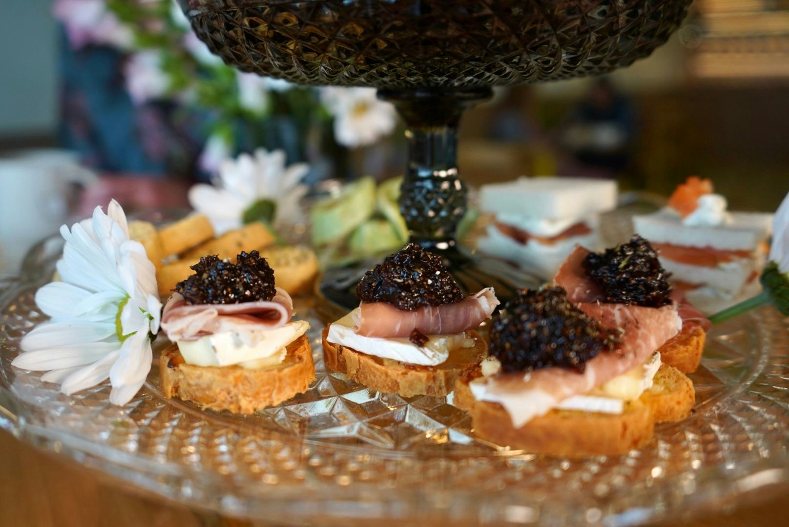 Crostini with Prosciutto, Brie and Balsamic Fig Jam and flowers on cake tray