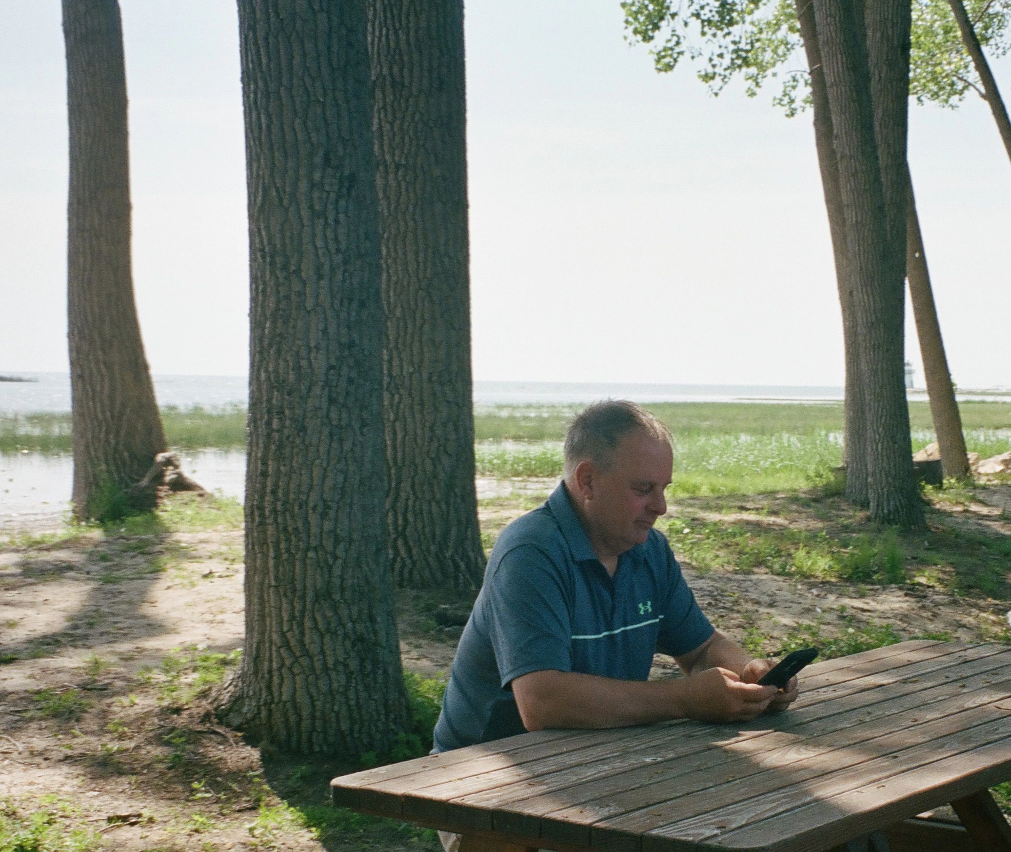 An operator checking his phone at a picnic table beside the water