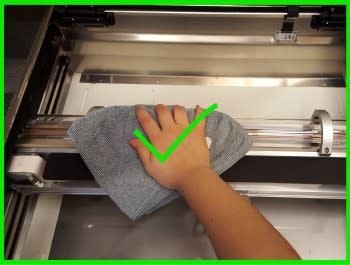 A hand cleaning the glass of the laser tube inside the Glowforge using a lint-free cloth.
