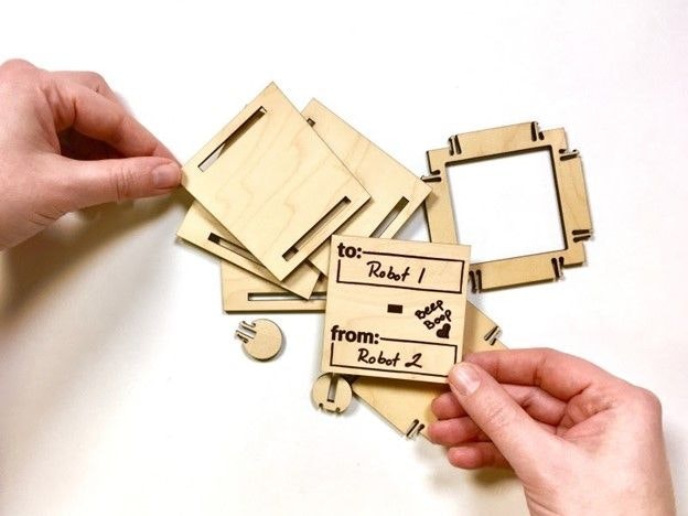 Two hands holding a lasercut wooden parts over a pile of other parts for a box prior to assembly