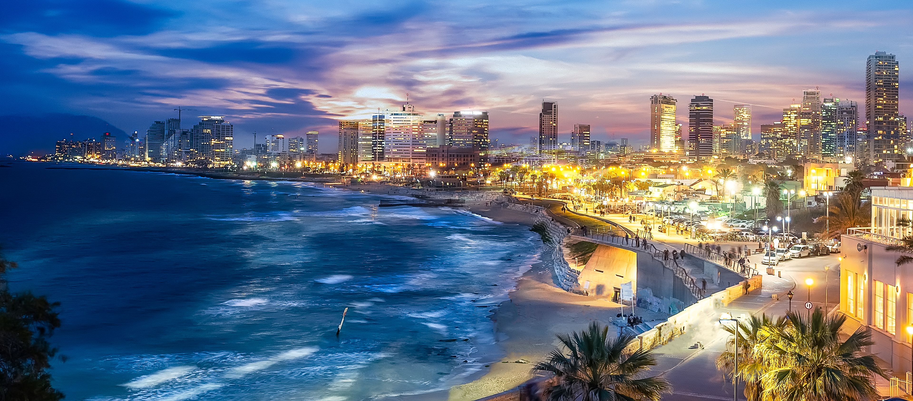 Esta imagem mostra uma paisagem urbana litorânea deslumbrante ao anoitecer ou ao amanhecer, com um vibrante horizonte da cidade com vários edifícios altos iluminados