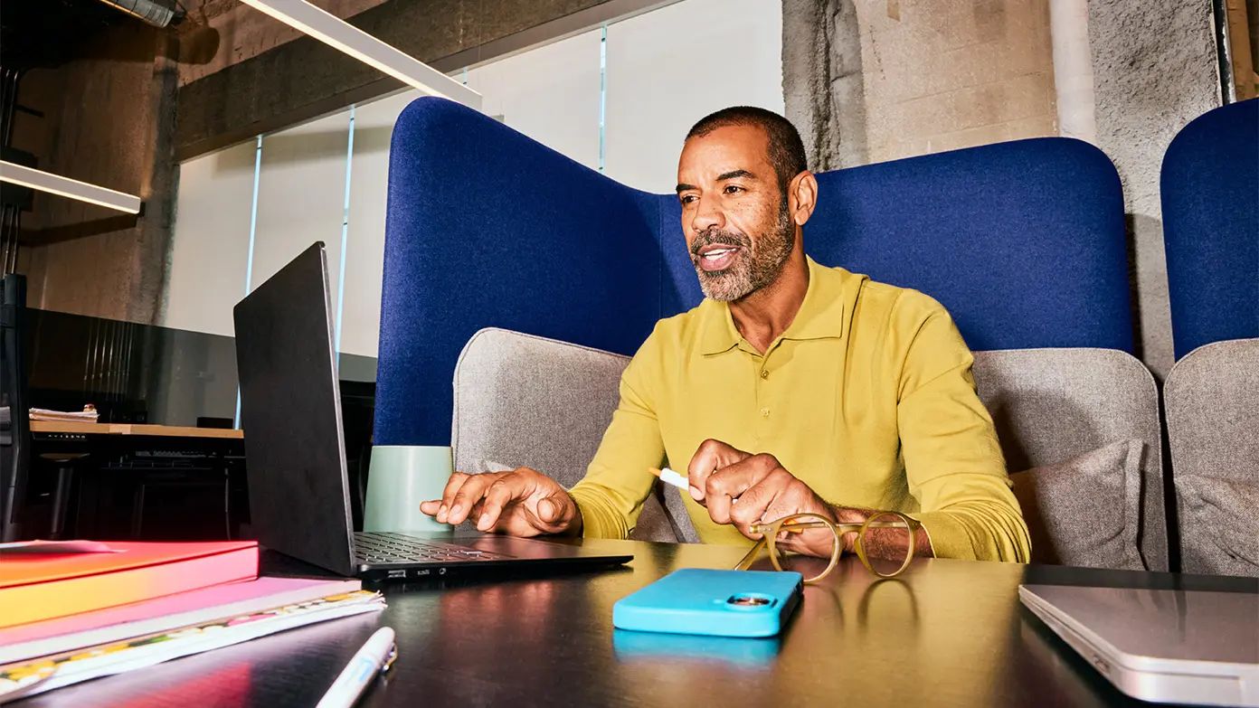 a man sitting in a modern office environment, engaged with a laptop placed on a desk.