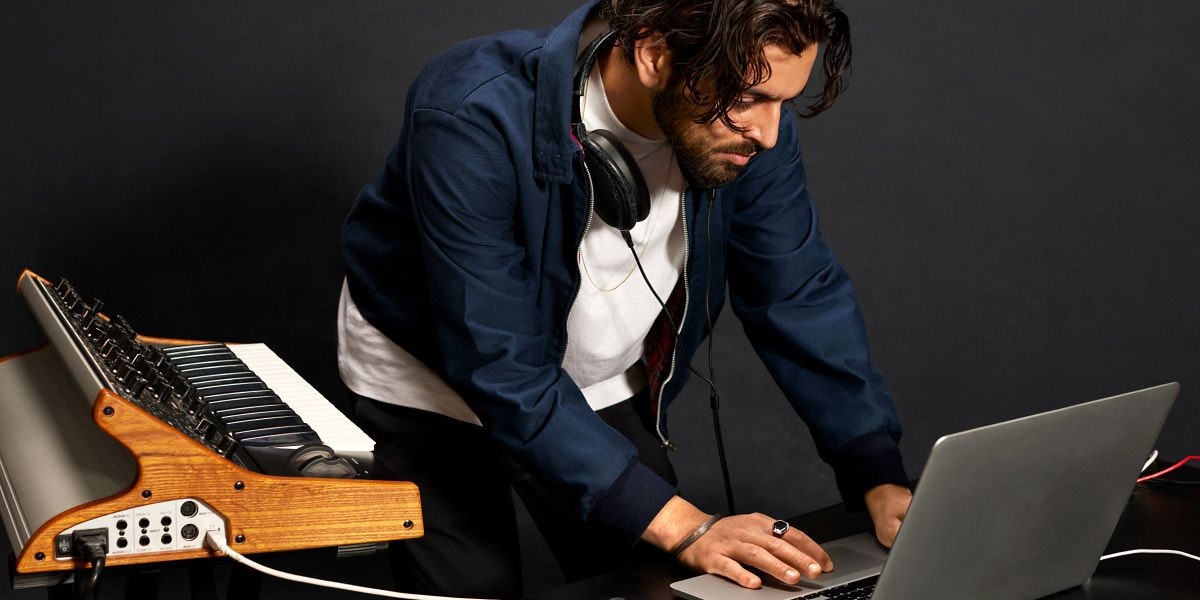 Person with headphones around neck, using laptop with a home studio setup