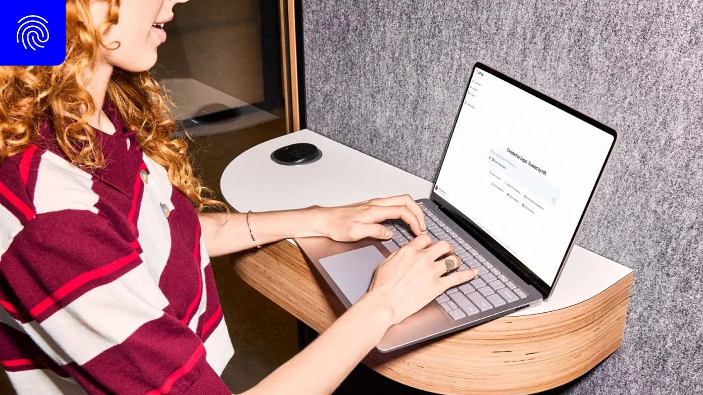 a person sitting at a wooden desk and typing on a laptop.