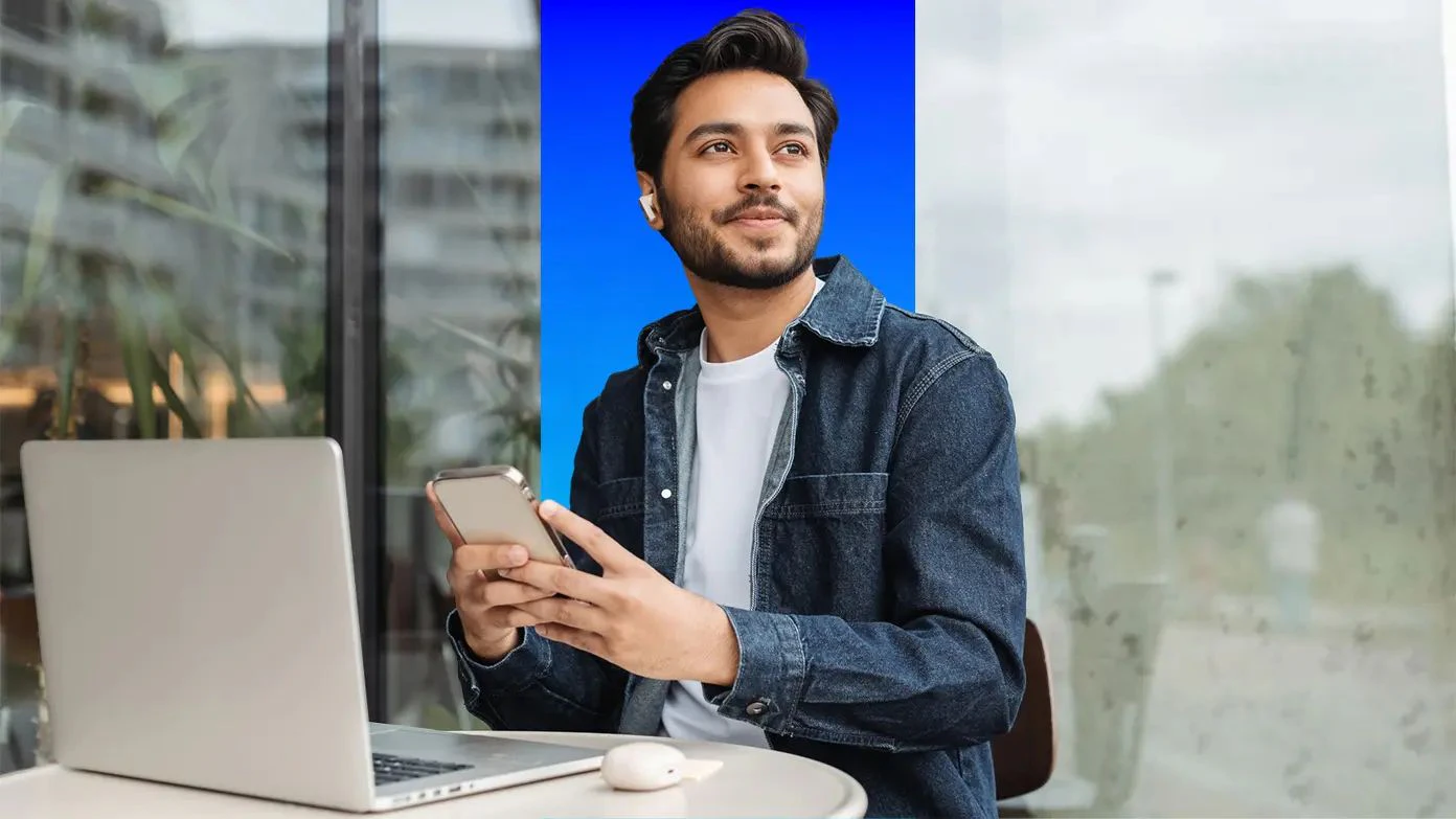 man sitting at desk with computer and typing on cell phone