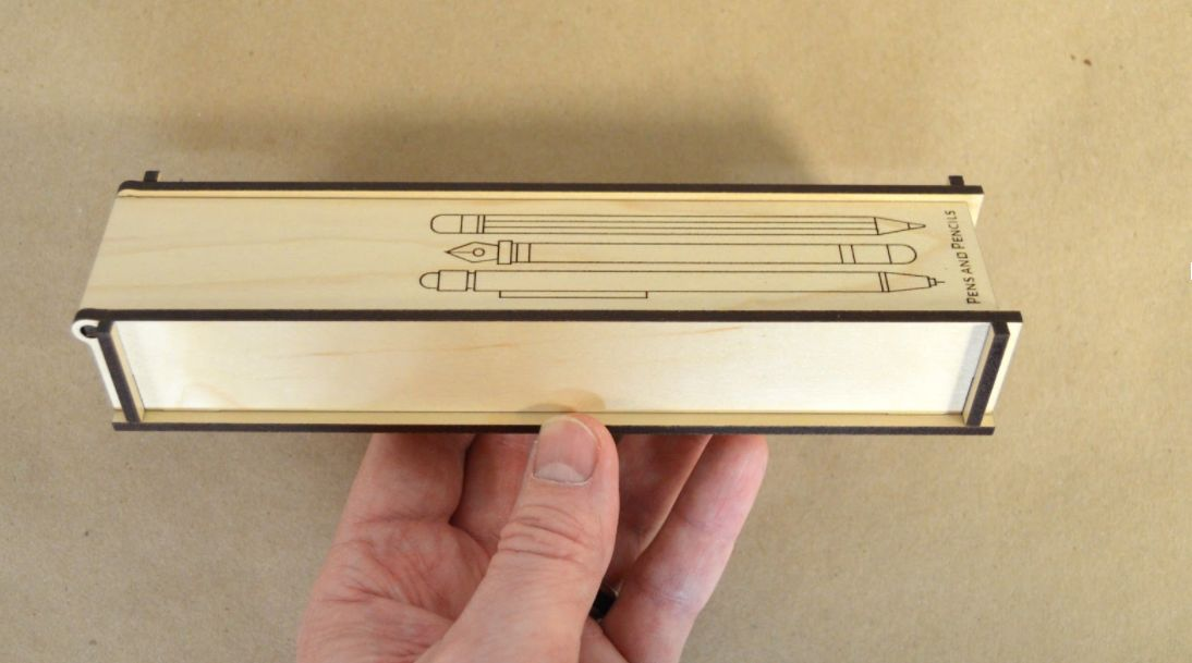 a hand holding a completed, laser cut wooden pencil case