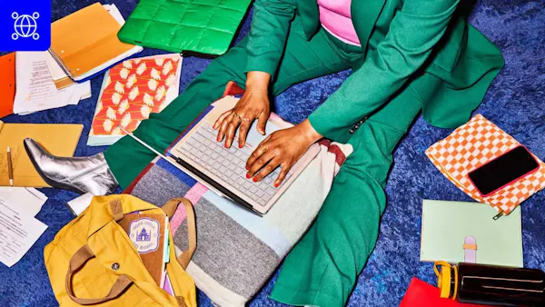 This image shows a person sitting on a blue carpet, surrounded by various items. 