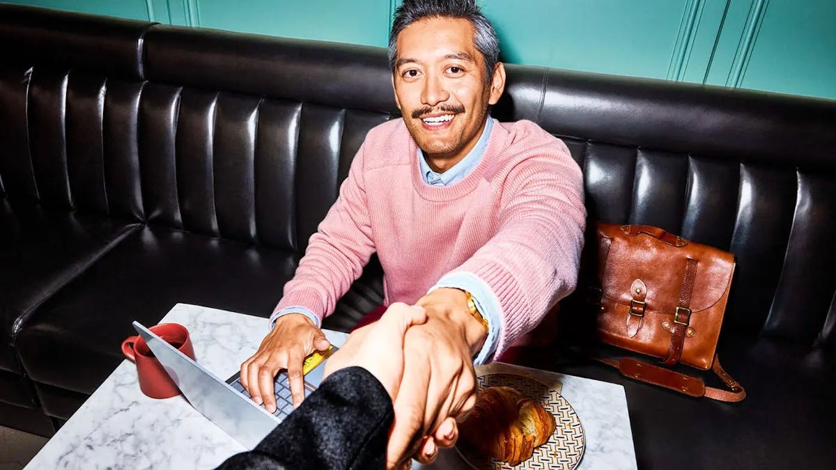 man working on computer and reaching up to shake another persons hand