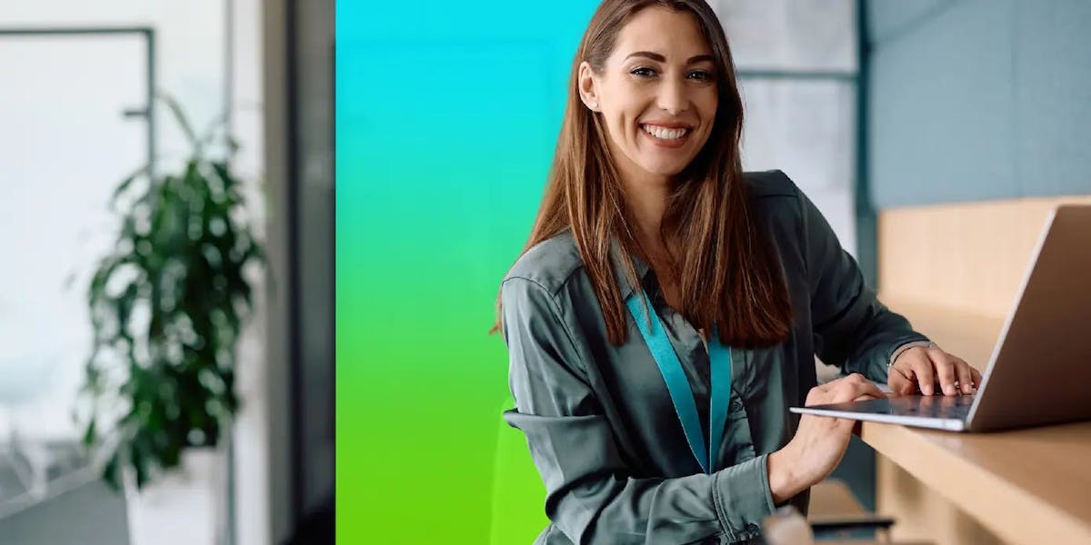 A woman in an office smiles while working on a laptop.