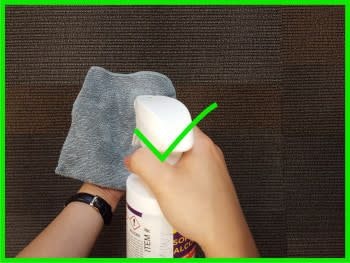 One hand holding a lint-free cloth while the other sprays isopropyl alcohol on the cloth