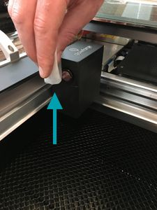 A hand holding a lens wipe and cleaning the window on the side of the Glowforge print head