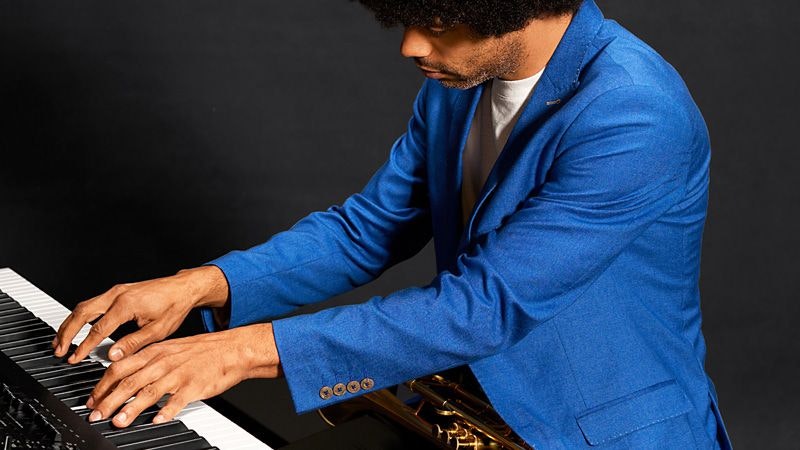 Person wearing a blue blazer, and playing an electric piano.