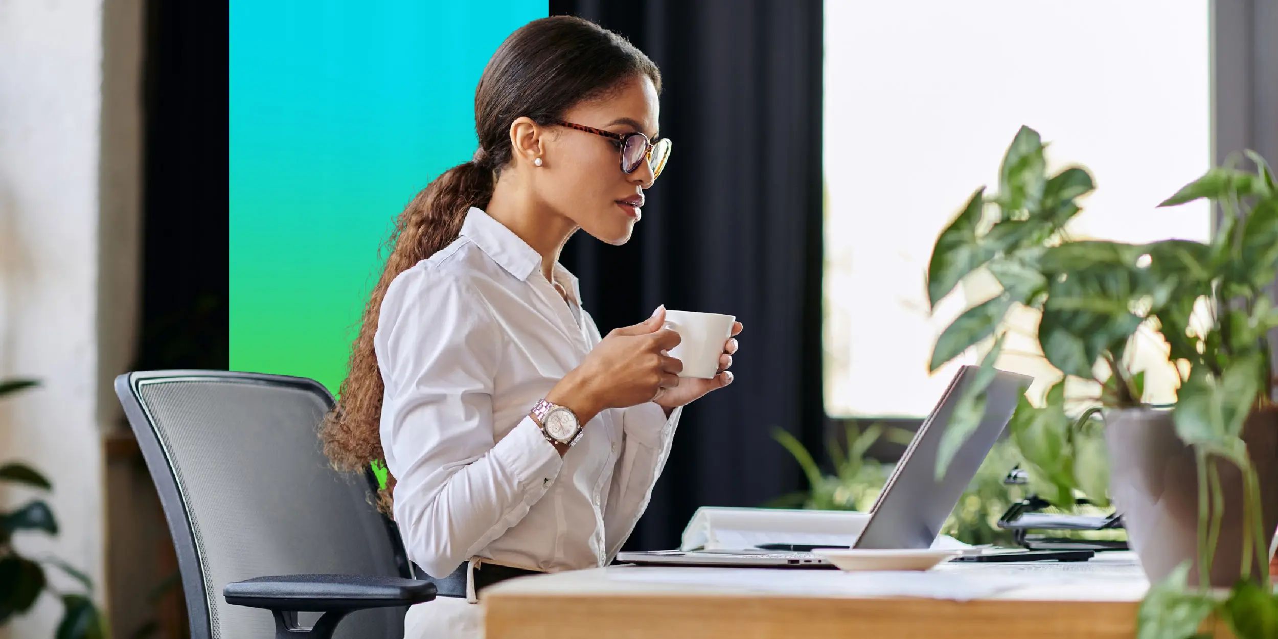 Employee at a desk drinking coffee while working on a laptop.