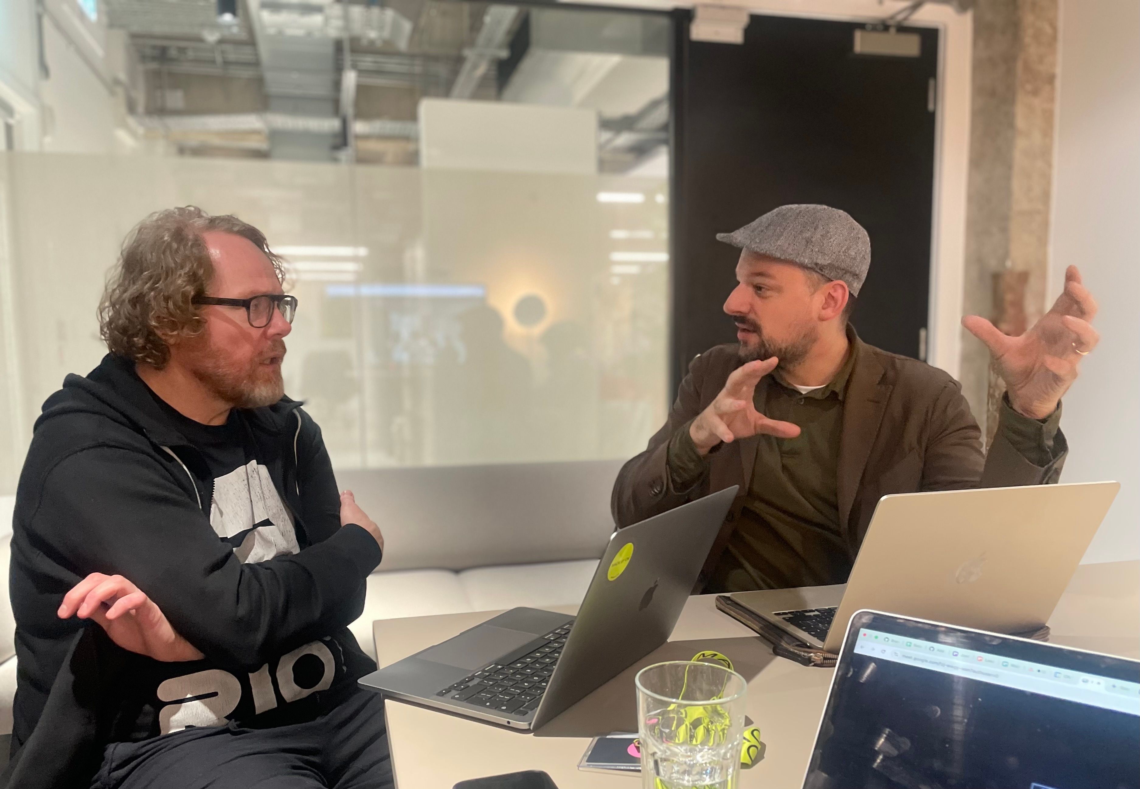 Two of the team in animated working discussion across a table, laptops open between them