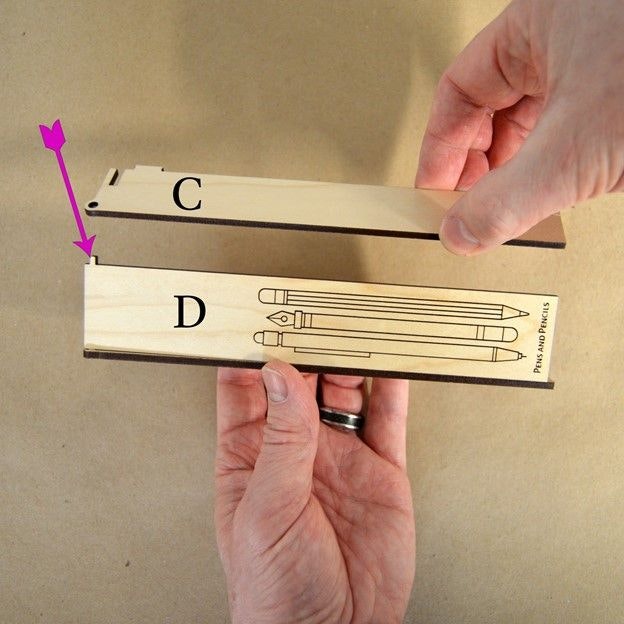 Two hands connecting wooden laser cut parts. The tab on part D is going into the hole on part C