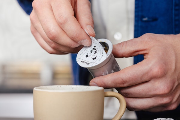 Hands peeling a Cometeer capsule over a mug
