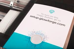 Button on the top of the Glowforge, with a paper card around it prompting owners to access the setup site