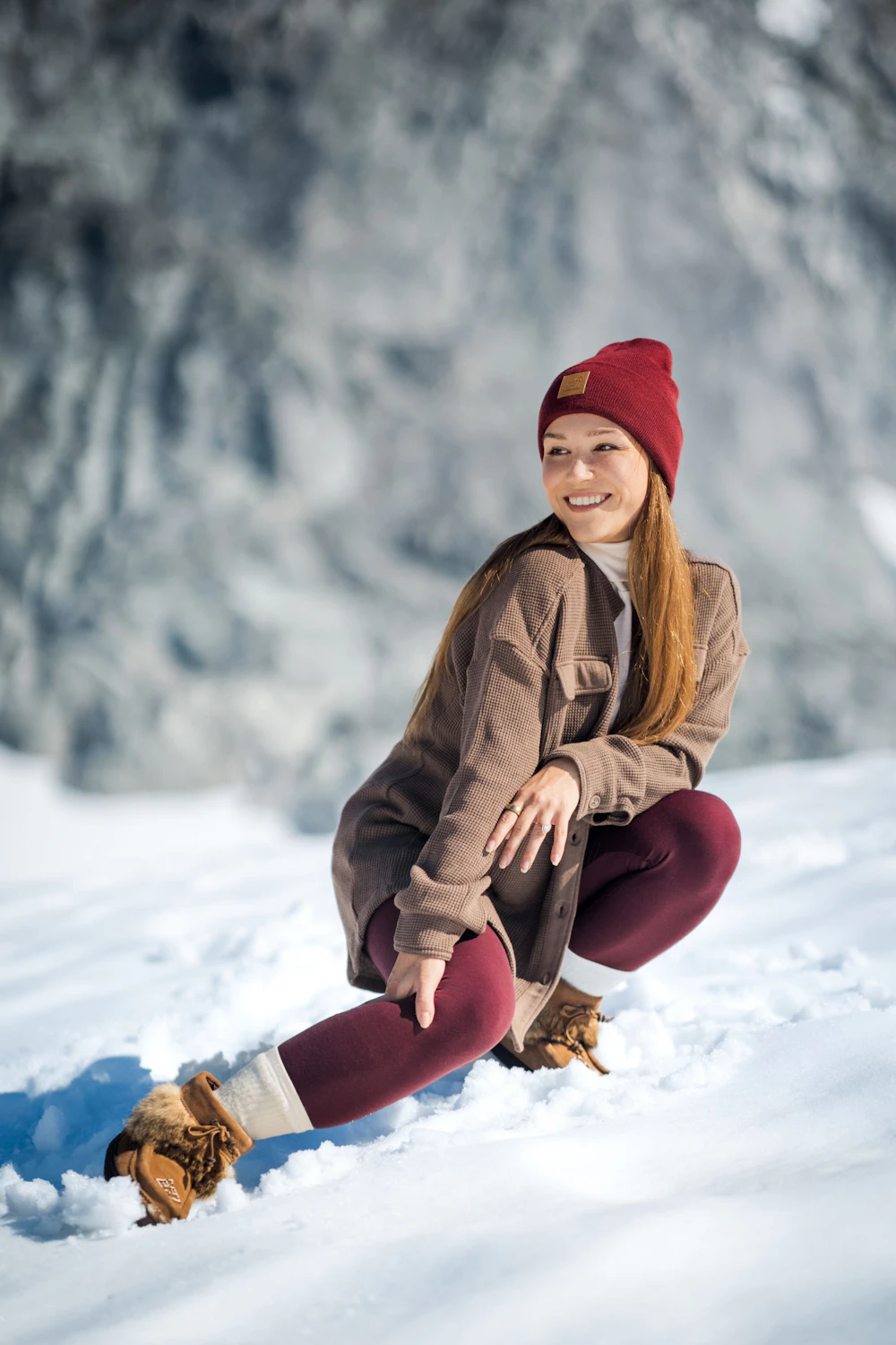 Woman wearing a red Woolx Baylor beanie, brown Oaklynn shacket and burgundy Stella leggings in a snowy mountain landscape