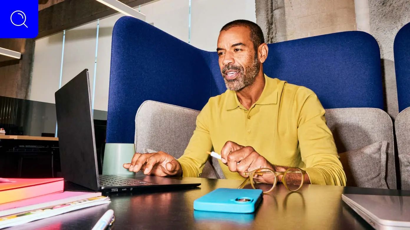 a man sitting in a modern office environment, engaged in work on a laptop​​ 