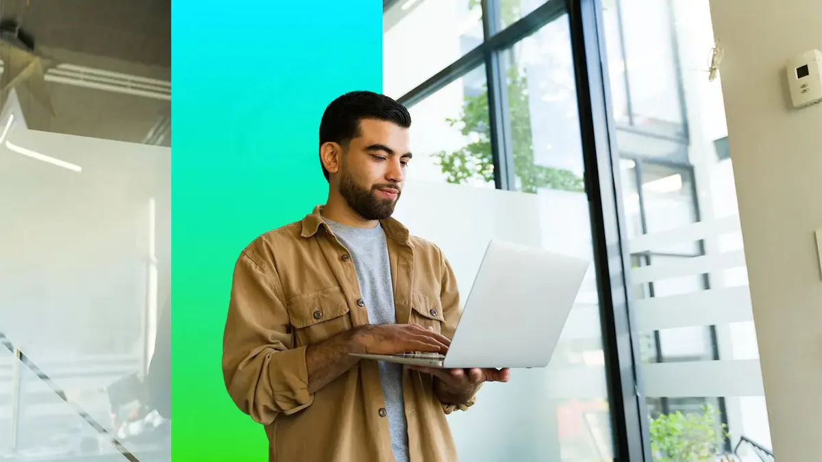 man standing in an office holding a laptop computer