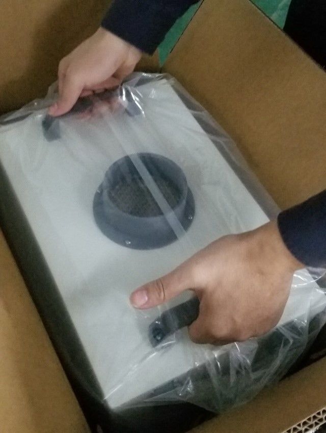 Two hands grasping handles on top of the filter unit and lifting it from the box.