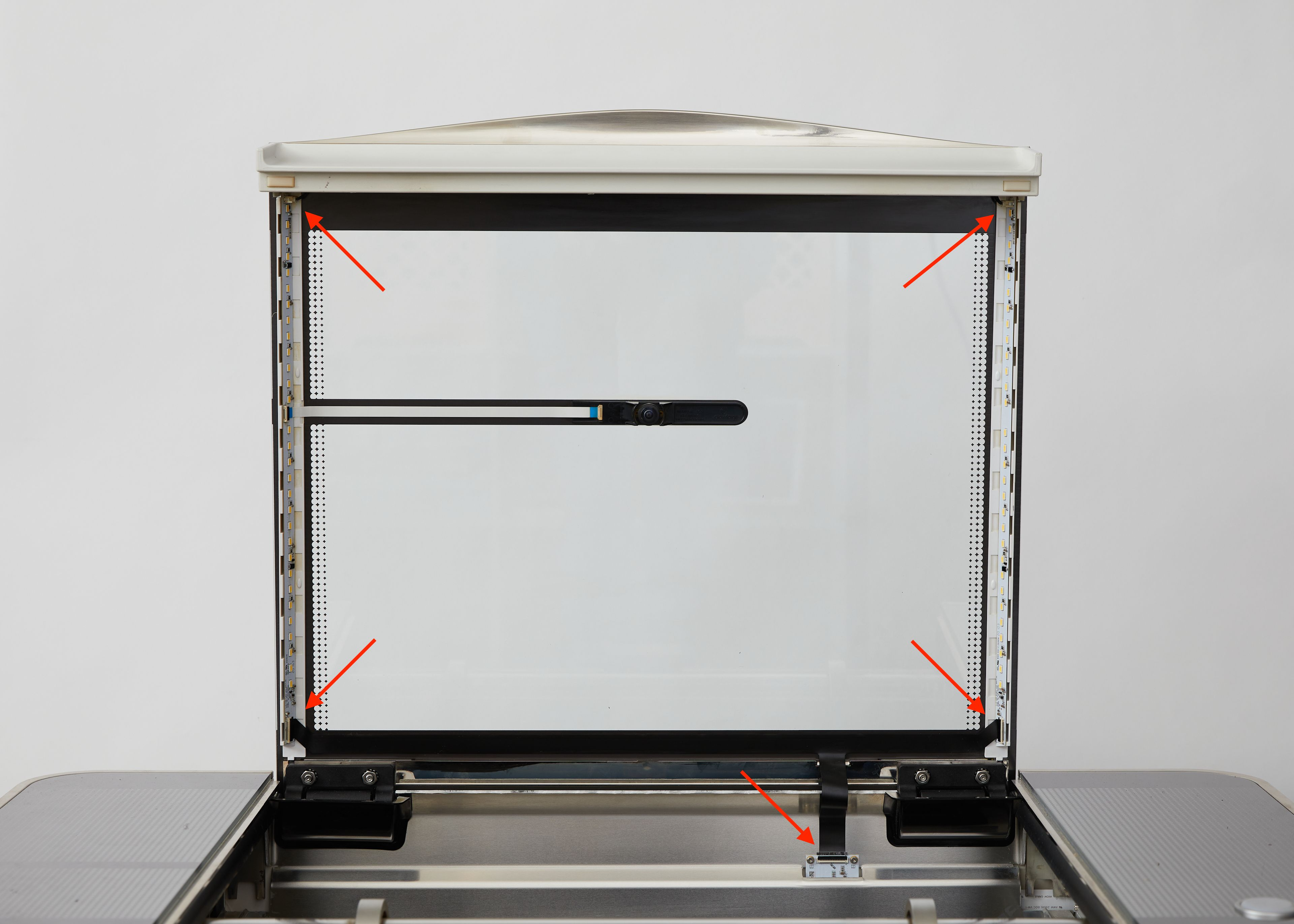A Glowforge with its lid open. The 3 connections on the black lid cable near its hinge and the 2 connections on the white lid cable leading to the camera are circled.