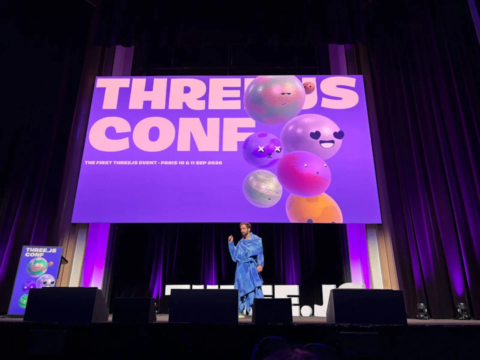 Conference creator David Ronai on stage in a blue robe, under a screen reading "Three.js Conf — the first Three.js event, Paris 10 & 11 Sep 2026"