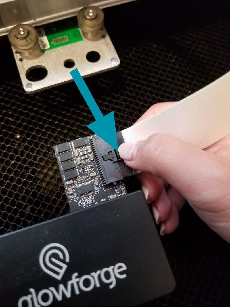 A hand disconnecting the wide, white ribbon cable from the Glowforge print head